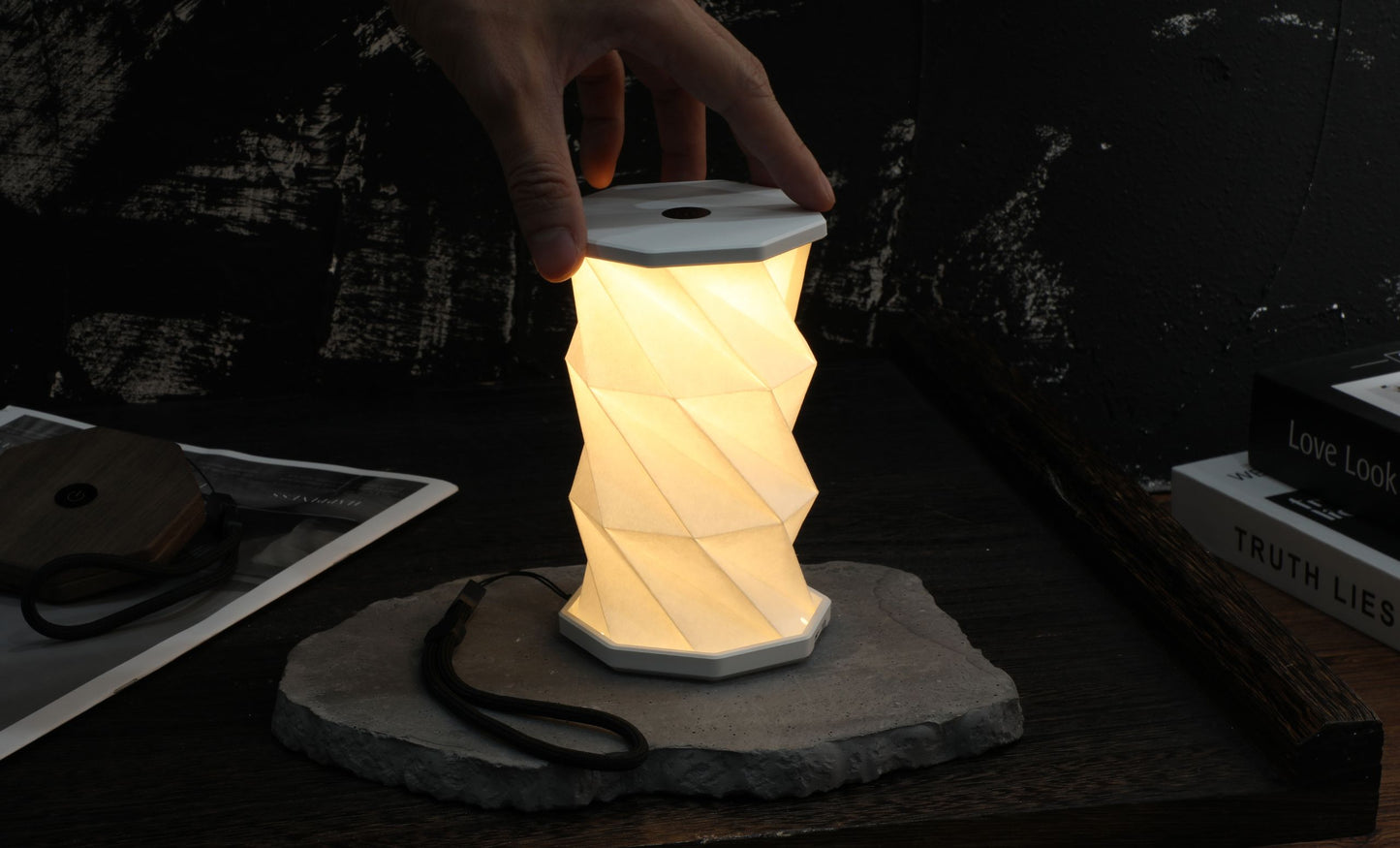 Foldable LED lamp being held by a hand on a dark surface